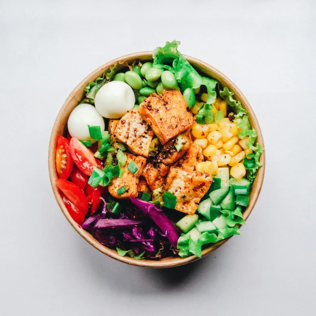 Bowl completo con hojas verdes, huevo, tomate, choclo y proteína