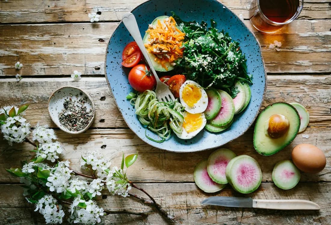 Plato azul con huevo poché, palta, tomate, rabanito sandía y verdes sobre mesa de madera