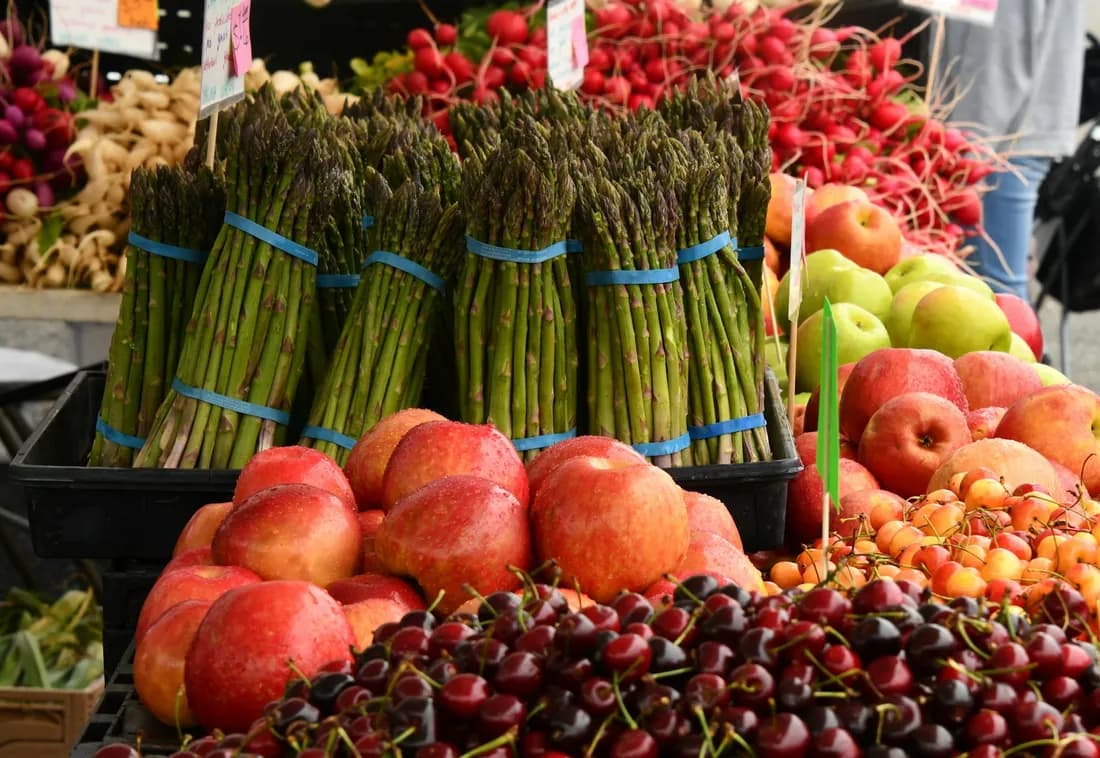 Puesto de feria con atados de espárragos, duraznos, cerezas y manzanas verdes